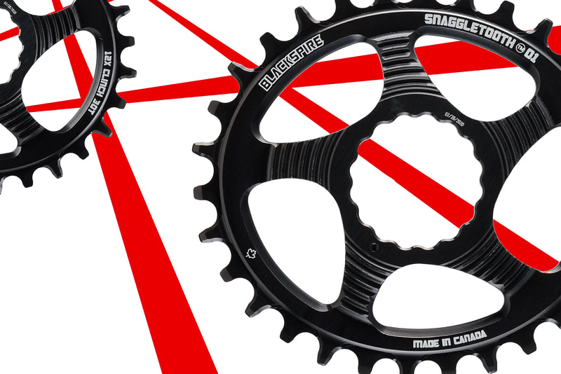 A pair of black bicycle chainrings in front of a white background with diagonal red lines. Shot by business photographer Mike Taylor in his Peterborough Ontario studio.