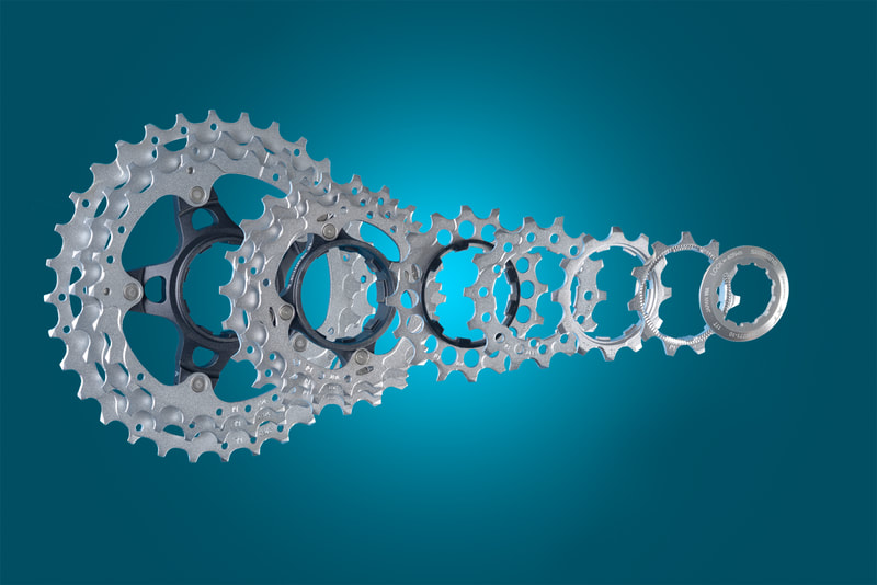 A bicycle gear cassette is shown in a disassembled condition against a gradated blue background. Shot by professional business photographer Mike Taylor in his Peterborough Ontario studio.