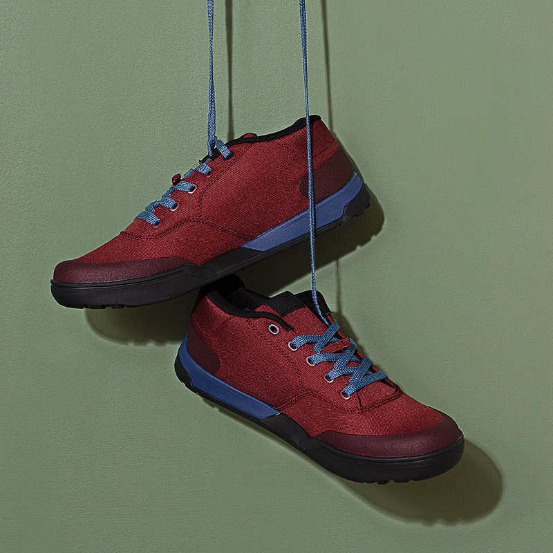 A pair of red shoes with blue laces are hanging in front of a green wall. Shot in studio by photographer Mike Taylor.