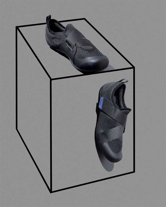 A pair of black cycling shoes are shown on an illustration of a grey toned cube.